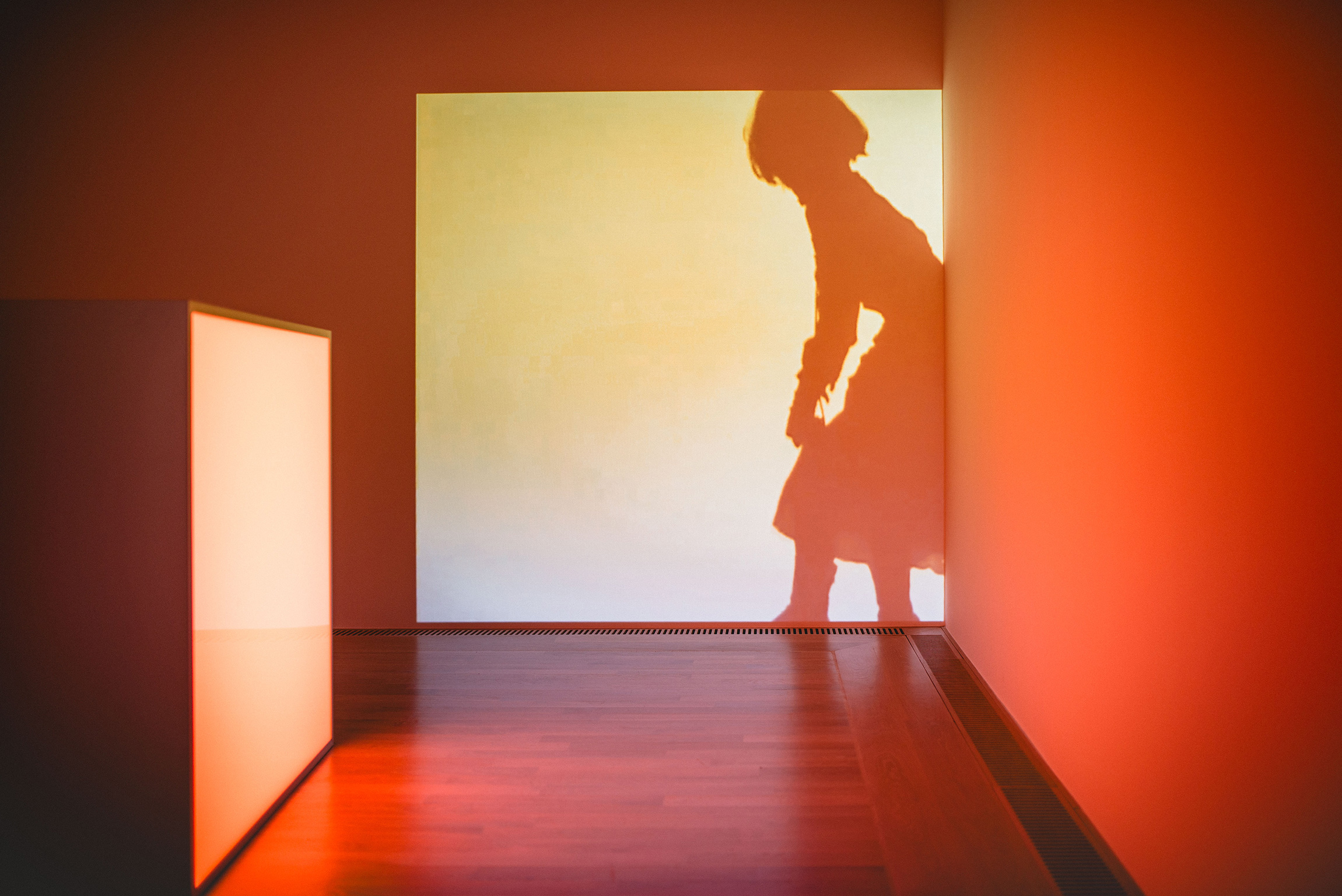 Das orangefarbige Bild zeigt eine schattige Silhouette einer Frau, die an einer Wand nach vorne gelehnt lehnt.
