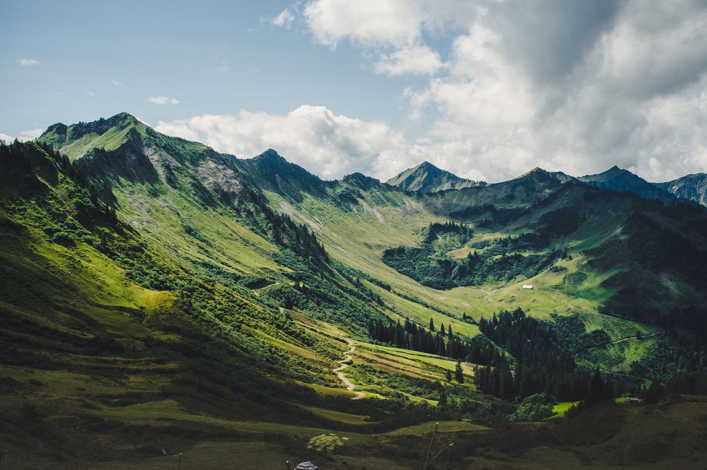 Der Blick schweift über einen Kessel mit einer einsamen Hütte. Im Hintergrund schroffe und satt grüne Berge