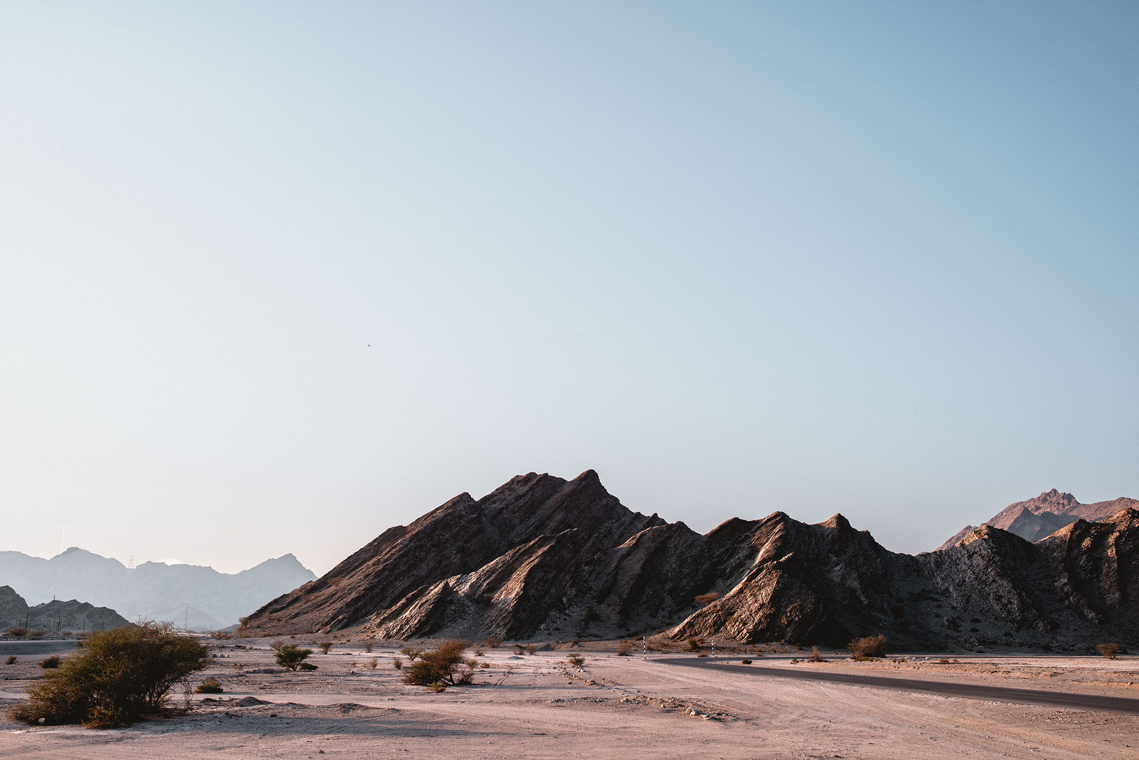 Ein Wüstenabschnitt im Oman. Im Hintergrund ein schroffes Felsmassiv.