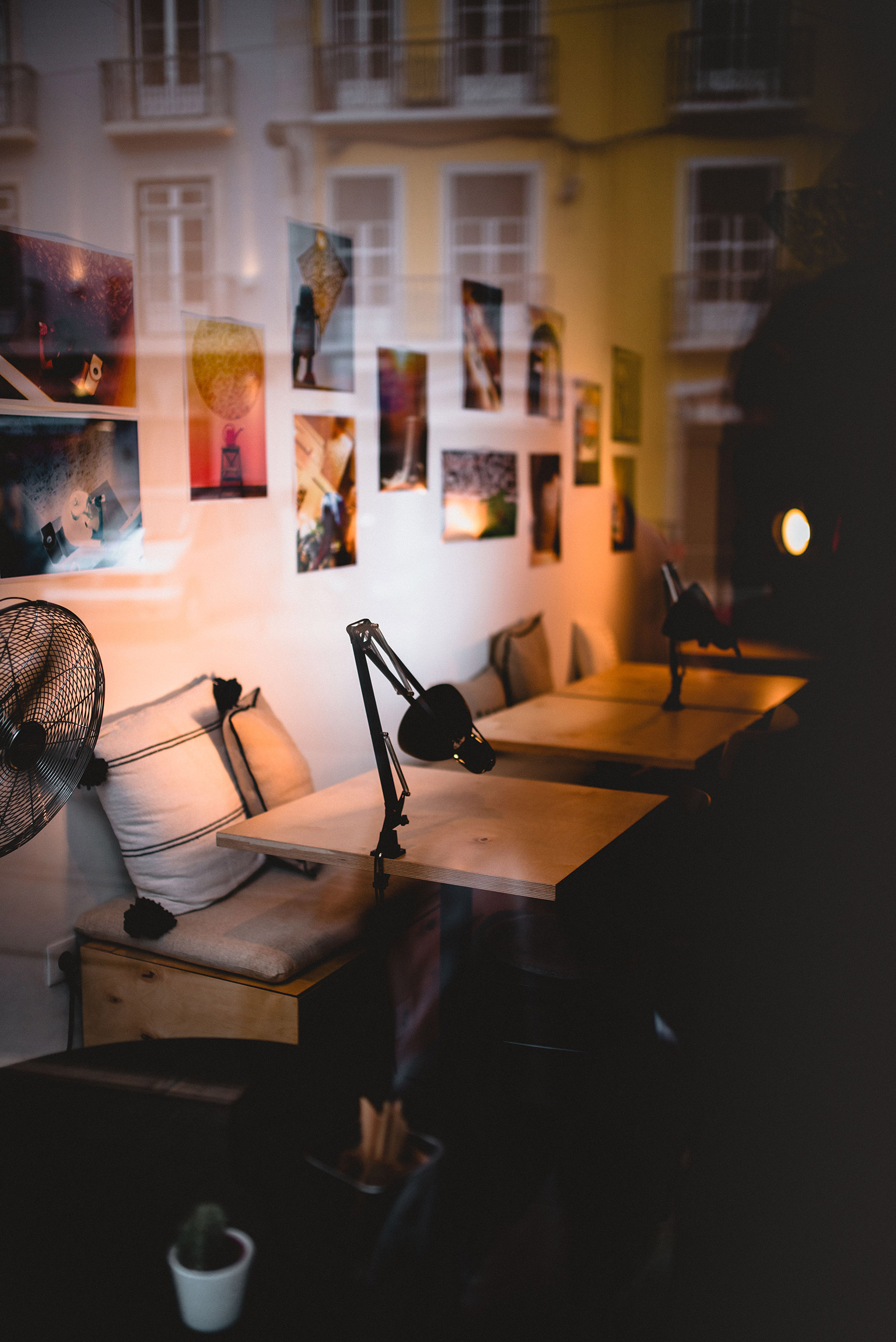 Blick von außen durch die Scheibe auf die Tische eines Cafes. An den Wänden hängen unzähligen Bilder.